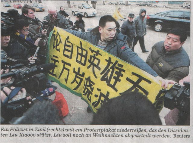 Chinese mit Protestplakat, umringt von Journalisten.
