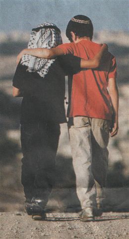 2 junge Männer, eine mit arabischer, einer mit jüdische Kopfbedeckung schreiten arm in arm eine Straße entlang
